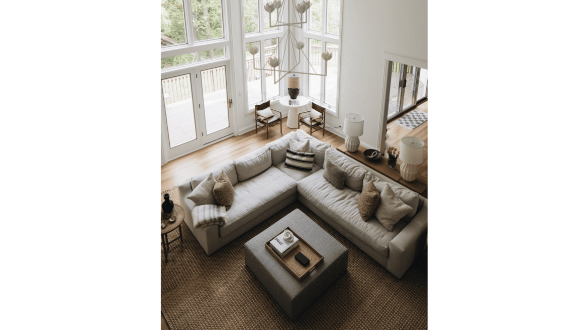 Sectional couch seen from above in white walled living room with two-story windows, white modern chandelier light fixture