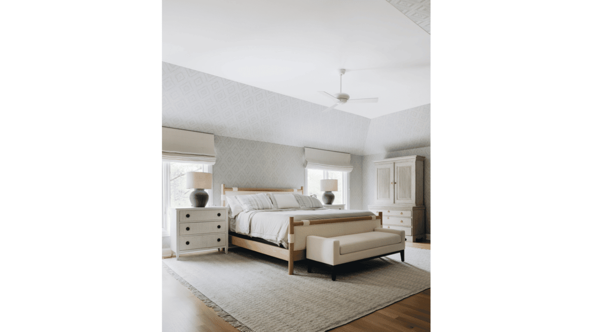 White primary bedroom with tray ceiling, wood floors, bedside tables and windows and white fan