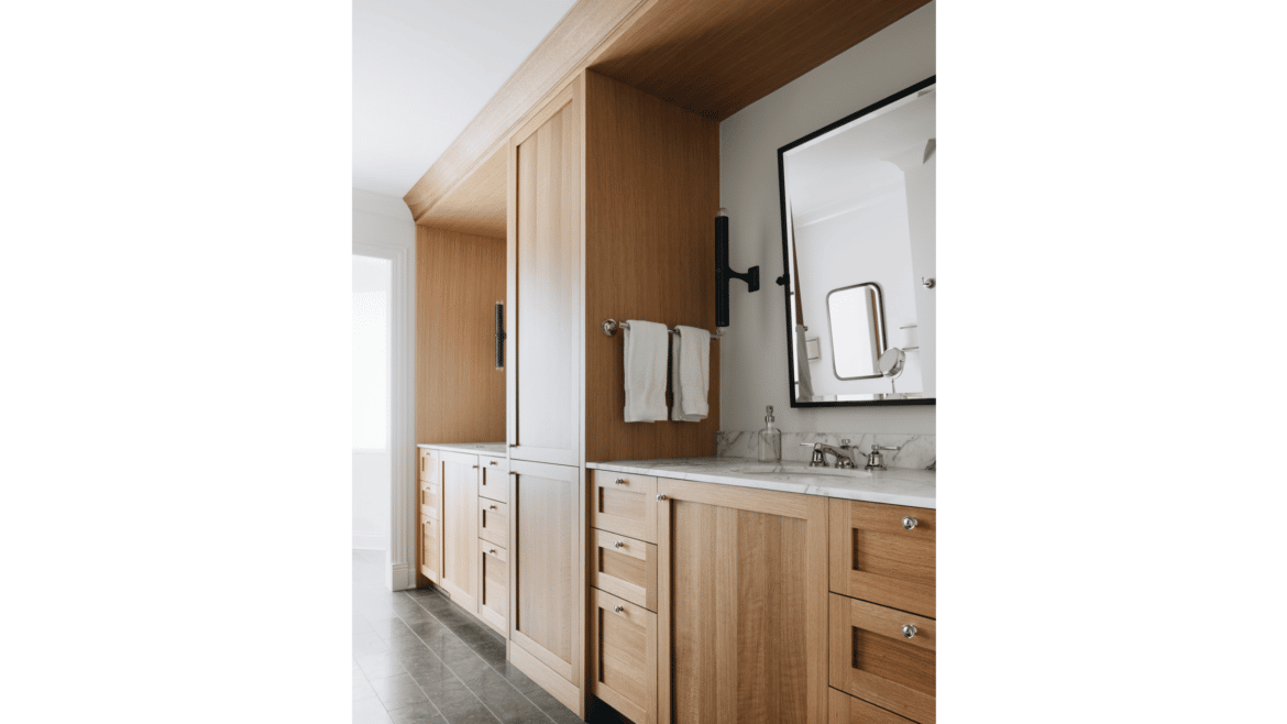 Double sink primary bathroom vanity with separate areas framed by light wood built-in cabinetry