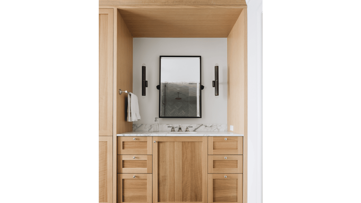 Primary bathroom vanity with gray marble countertop areas framed by light wood built-in cabinetry
