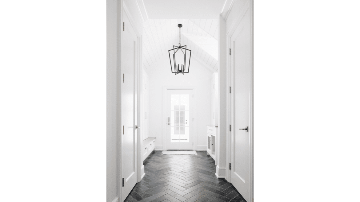 All white back foyer mudroom with large black metal hanging light fixture, black herringbone tile