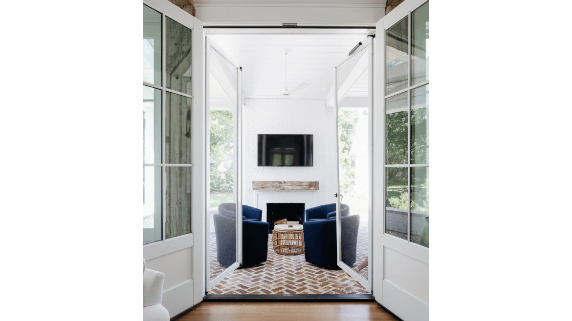 Doors open to outdoor patio - white seating with fireplace, overhead fan and white-washed red brick floor