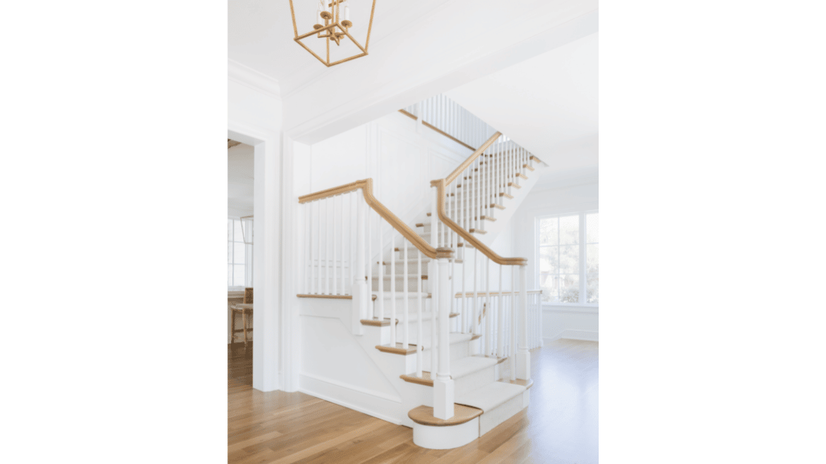 All-white front hall l-shaped stairs of farmhouse design with natural wood railing, floors and stairs