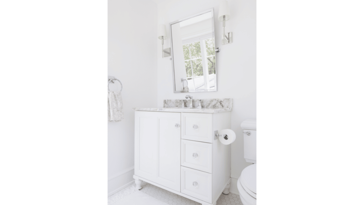 Farmhouse all-white powder room vanity with tilted mirror and lampshade sconces.