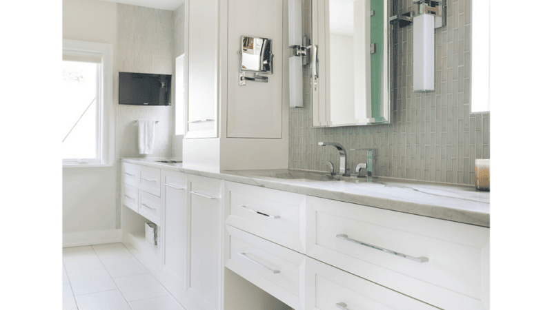 Double sink primary bathroom vanity with separate areas framed by white built-in cabinetry