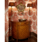 George Maher home wood bathroom vanity with in-wall faucets, vessel sink, deep red large-print wallpaper and large lampshade sconces