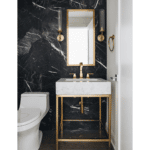 Brass and white marble powder room vanity with full wall black marble, brass sconces