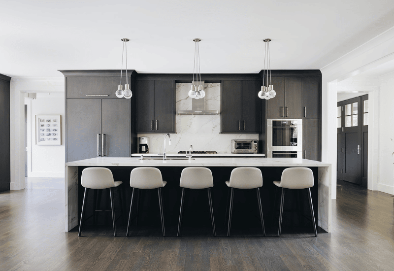 Modern craftsman kitchen with hanging light fixtures over a white top island with five seats and dark custom cabinetry