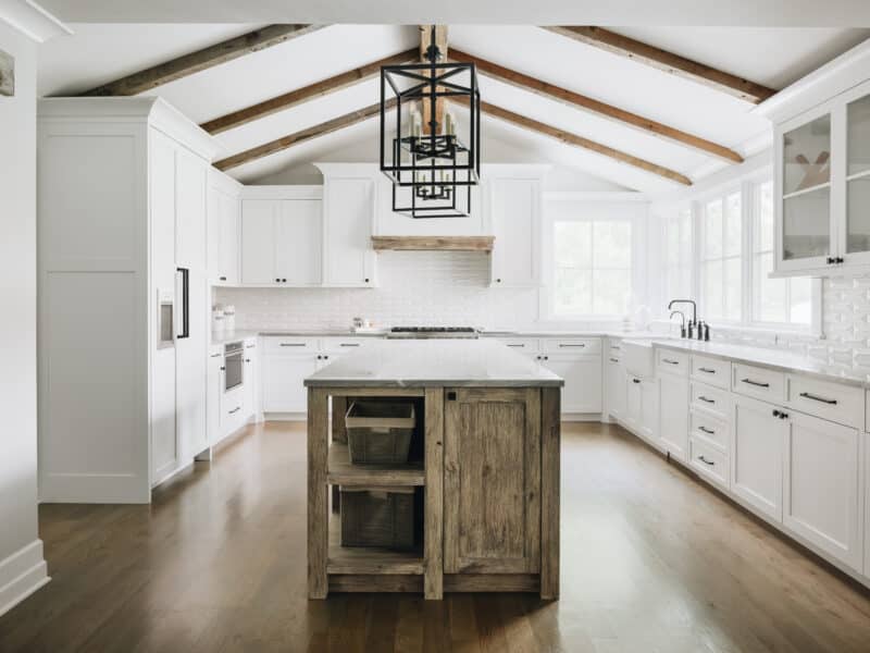 White low country farmhouse kitchen with reclaimed wood beam cathedral ceiling, white tile, white cabinets and wood foors