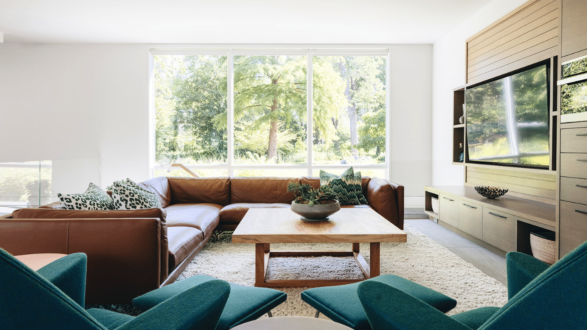 Modern design seating area with large screen TV, leather sectional, large windows to greenery